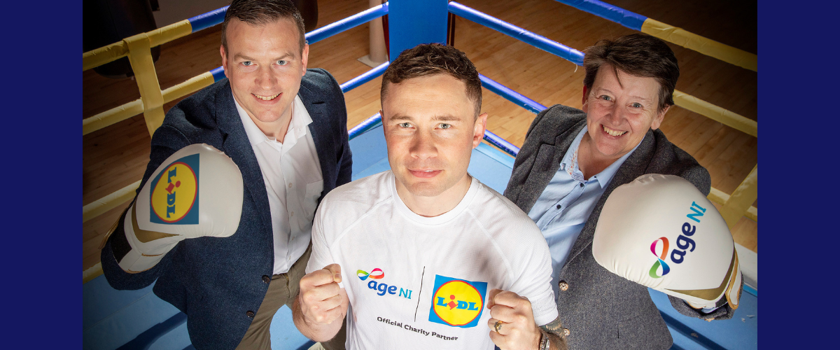 three people in a boxing ring with Age NI and Lidl logo boxing gloves