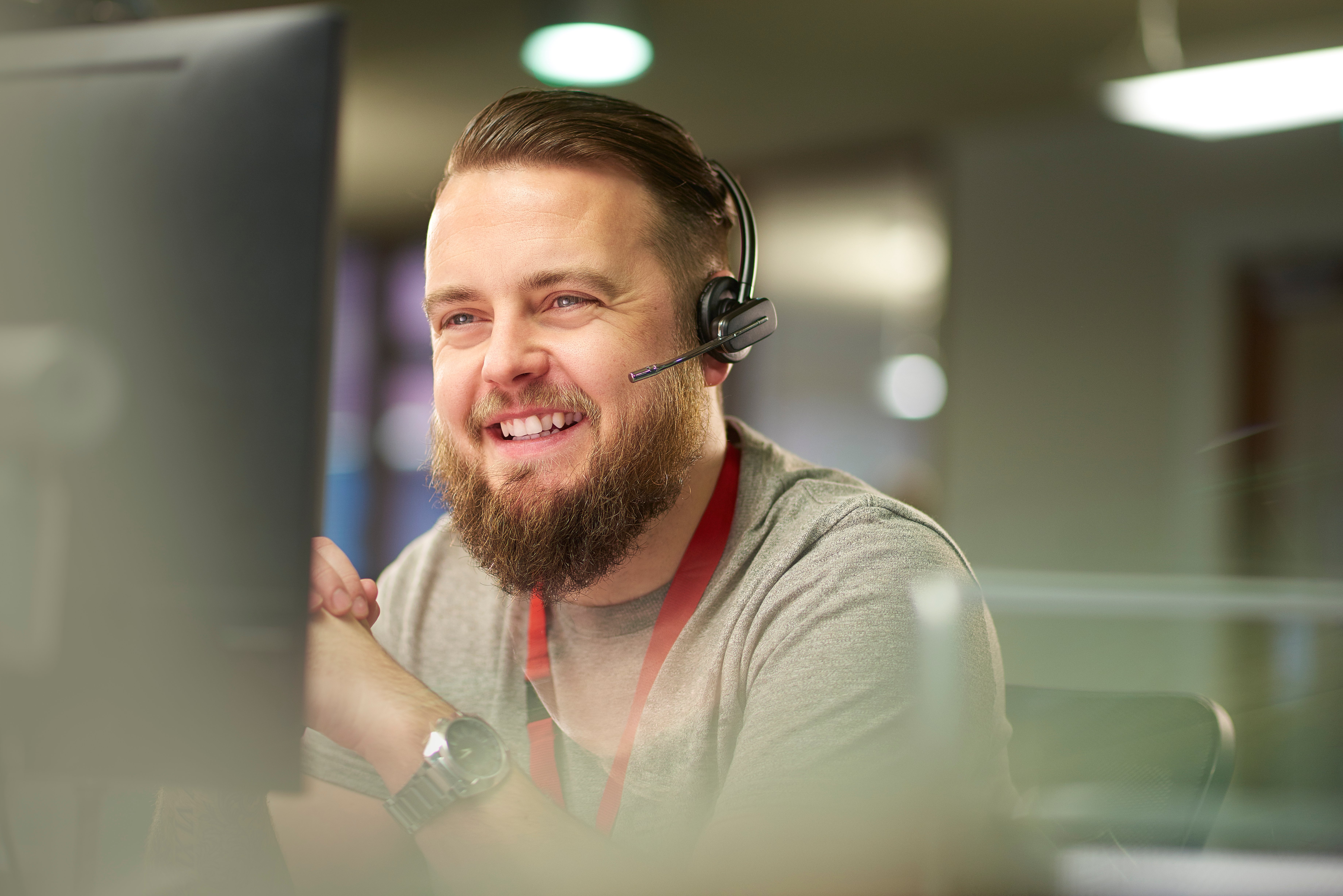 man in a call centre smiling while on the phone with computer on the foreground