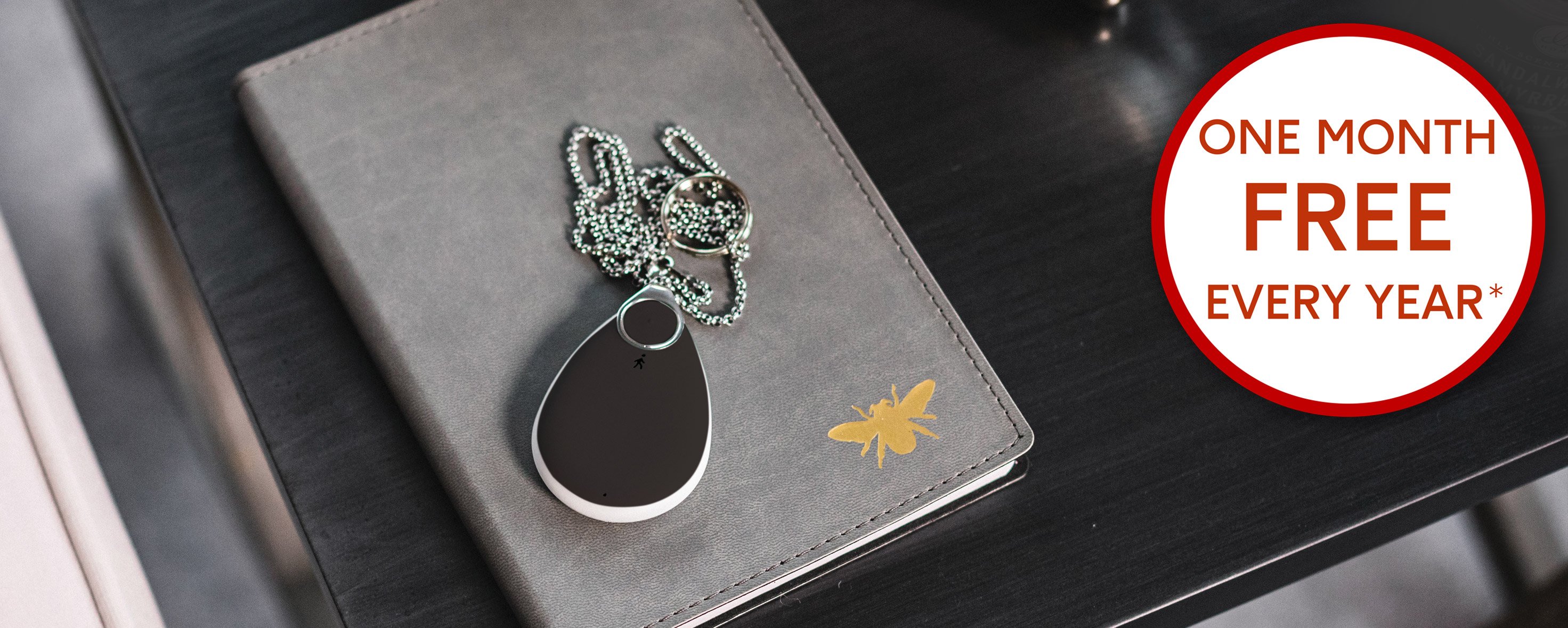 Fall alarm pendant sitting on a notebook on a desk, orange banner in corner "£40 off setup extended for a limited time only"